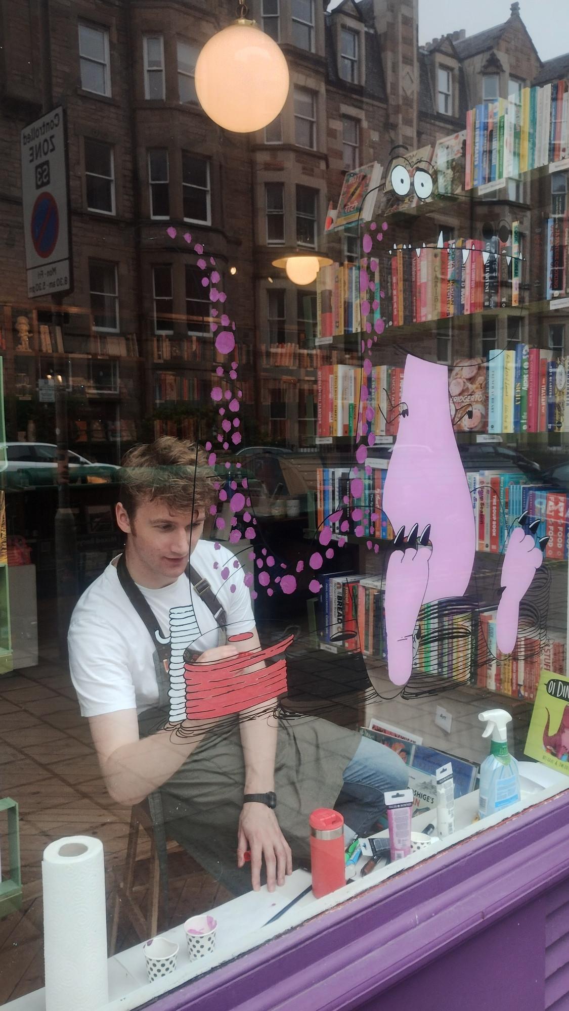 Looking in the window of the bookshop as bookseller Jack fills in some colour in the outline he's already drawn on the window glass