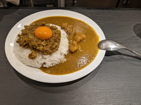 丸い皿に乗ったカレーライス。海の部分にはチキンカレー、ライスにはキーマカレーが載り、卵黄も載る。